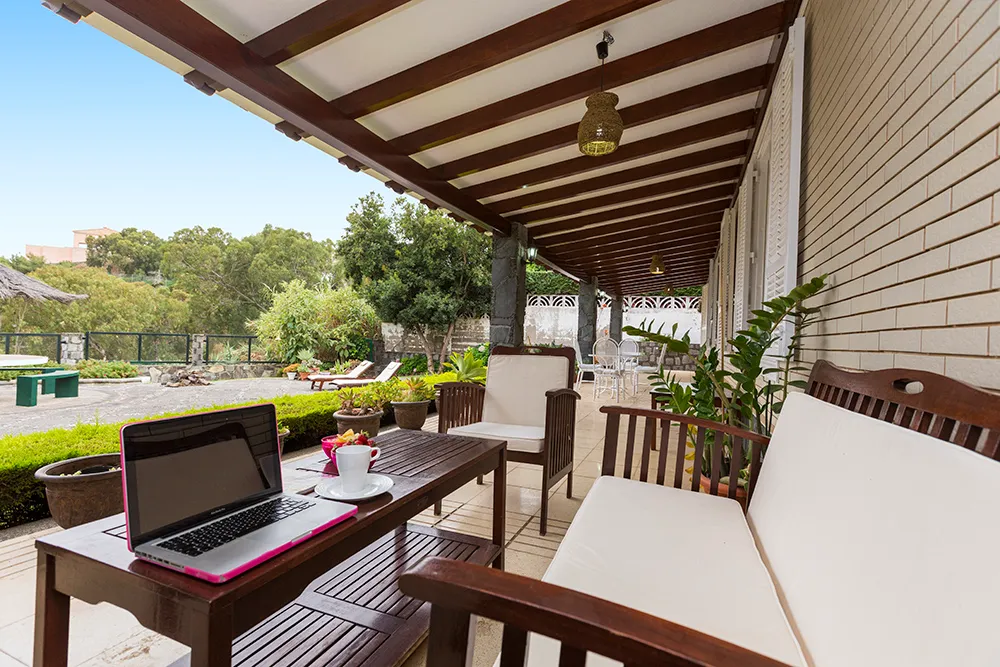 Terraza cubierta con banco de madera y vistas a un jardín arbolado en la casa Atalaya.