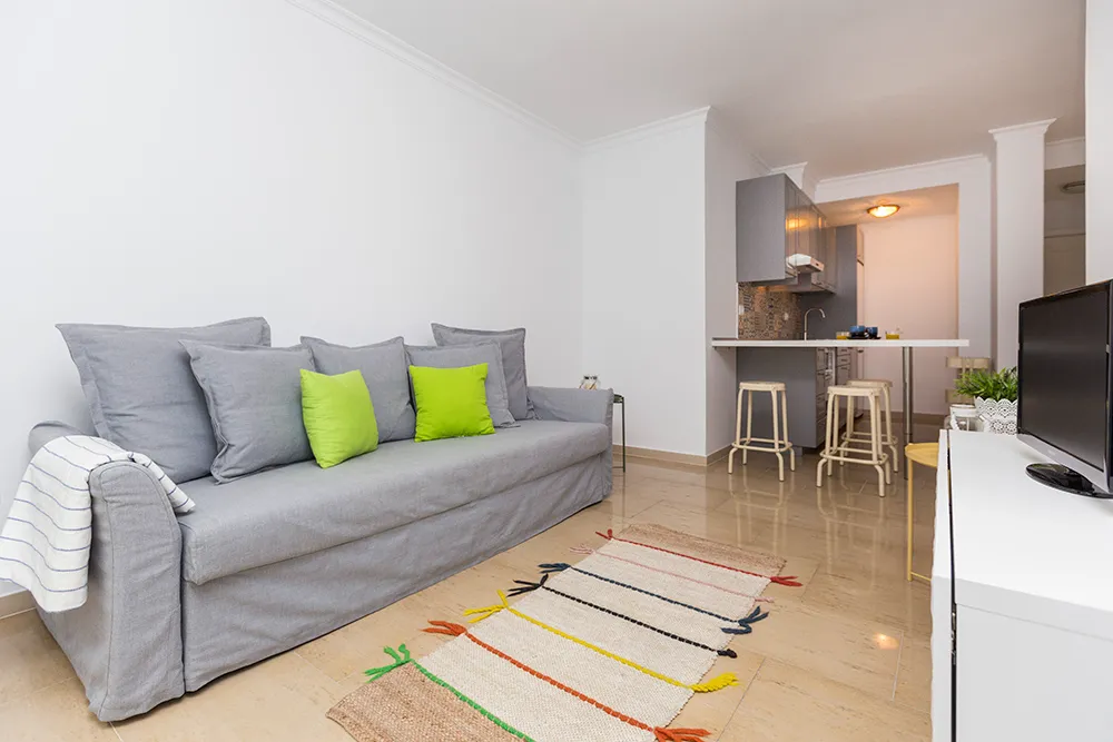 Salón luminoso con sofá gris y cojines verdes del apartamento en Las Canteras.
